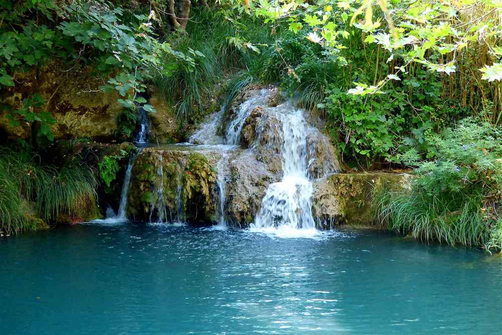 A lower cascade of the Polylimnio waterfalls spilling over mossy rock into a turquoise pool