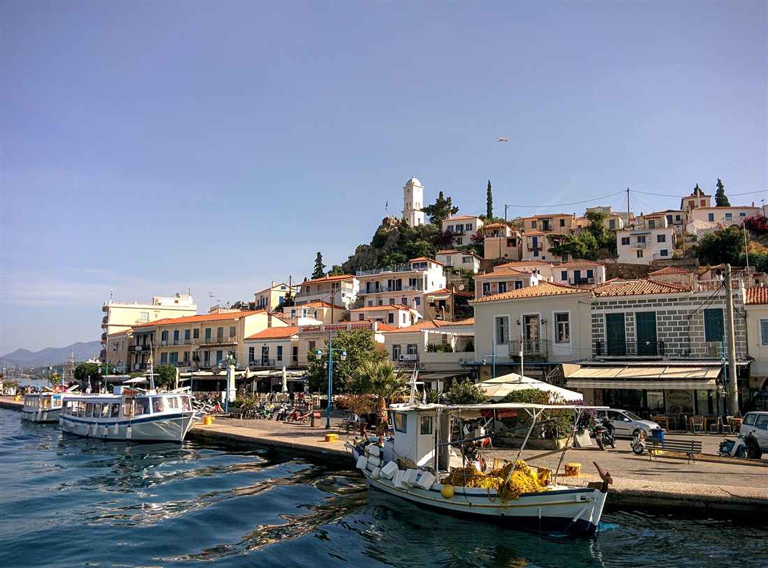 The waterfront of Poros Town with its white clock tower on the hill above the moored boats, a base for a Poros yacht charter