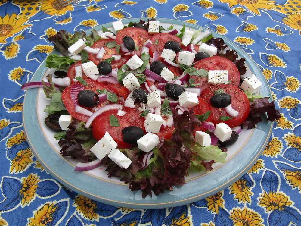 A Greek salad of sliced tomatoes, feta, red onion and black olives dressed with olive oil