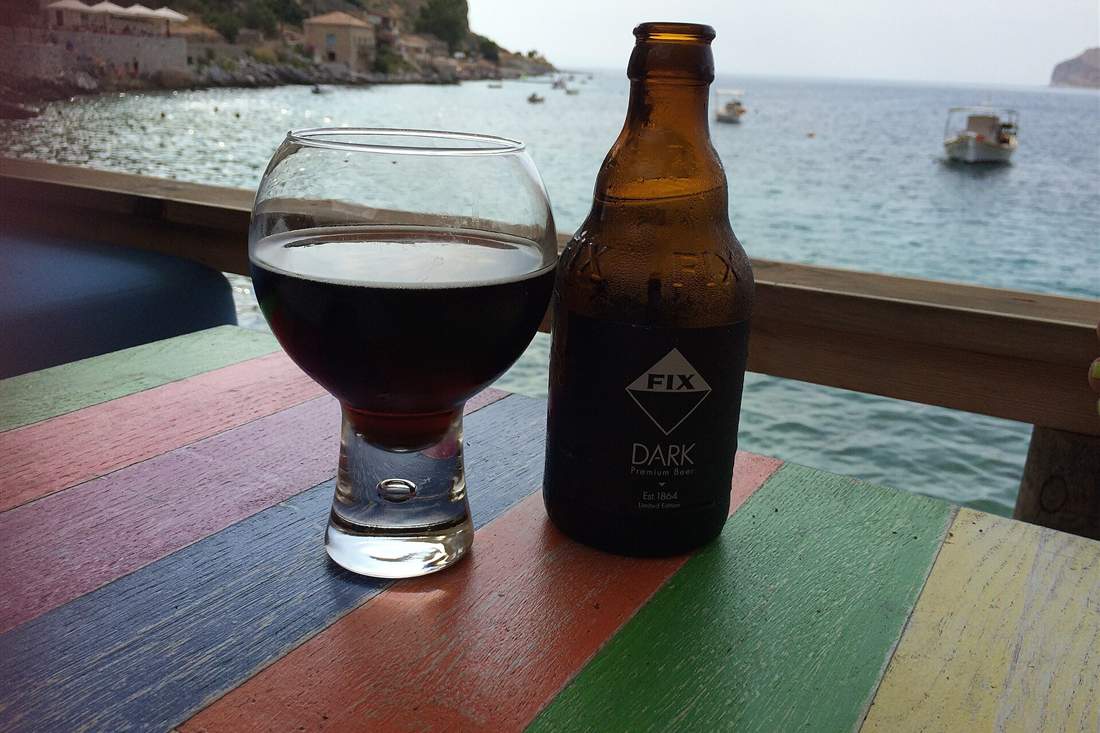 Santorini beer tasting: a glass of dark Greek craft beer and its bottle on a seaside table