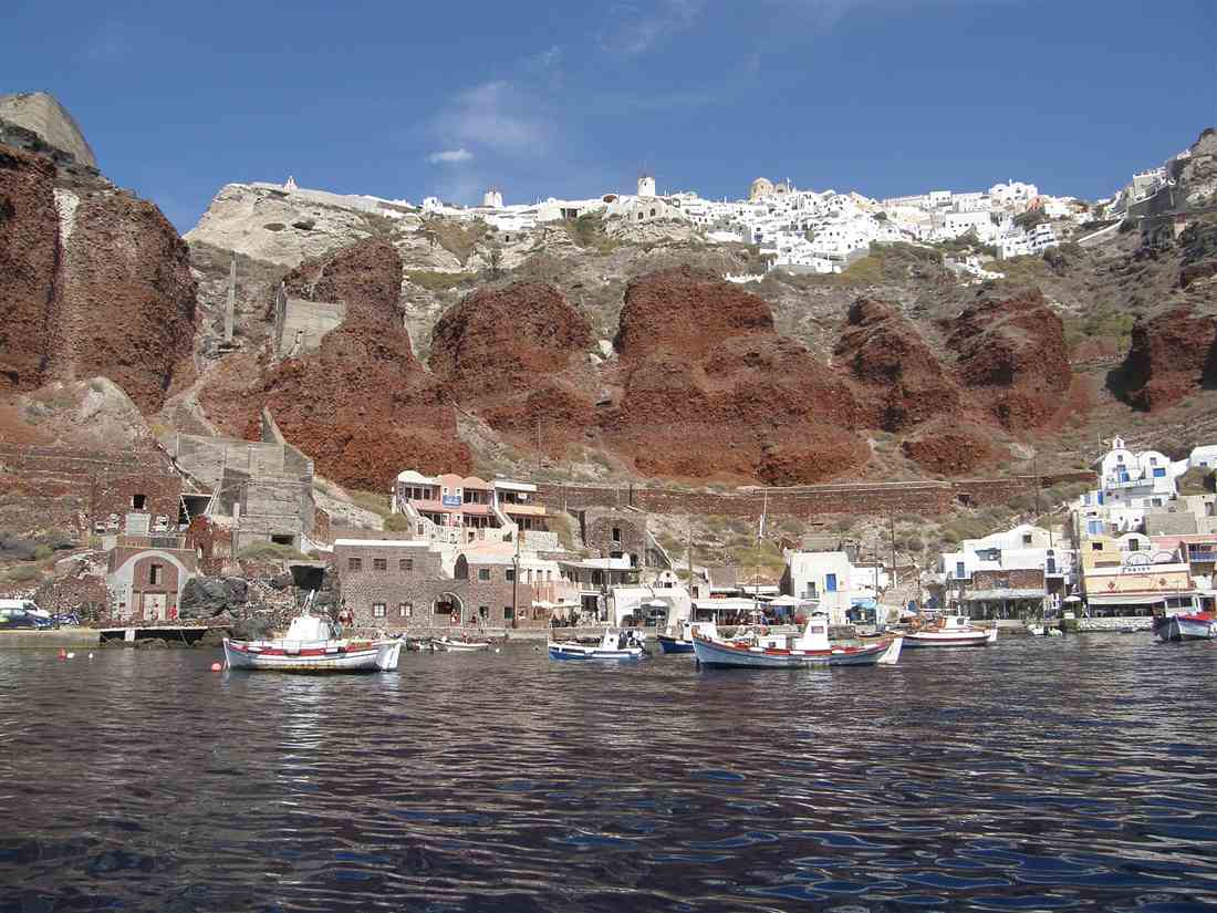 Amoudi Bay and the red cliffs below Oia seen from the water, the caldera stretch a Santorini catamaran cruise sails