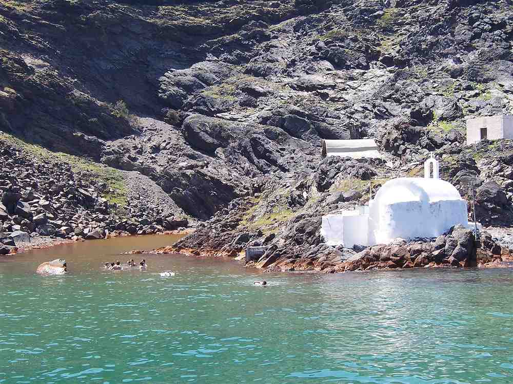 Swimmers in the warm ochre water of the hot springs at Palea Kameni beside the white chapel