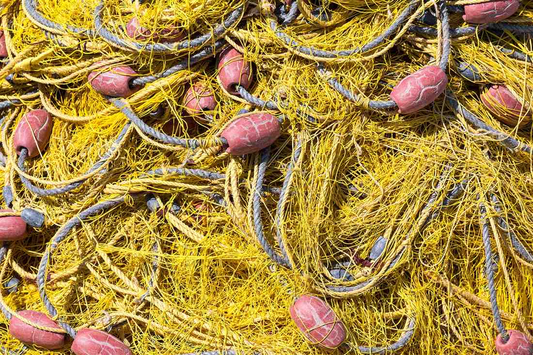 Yellow fishing nets and red floats stacked on the quay at the Vlychada marina, the working gear of Santorini fishing trips
