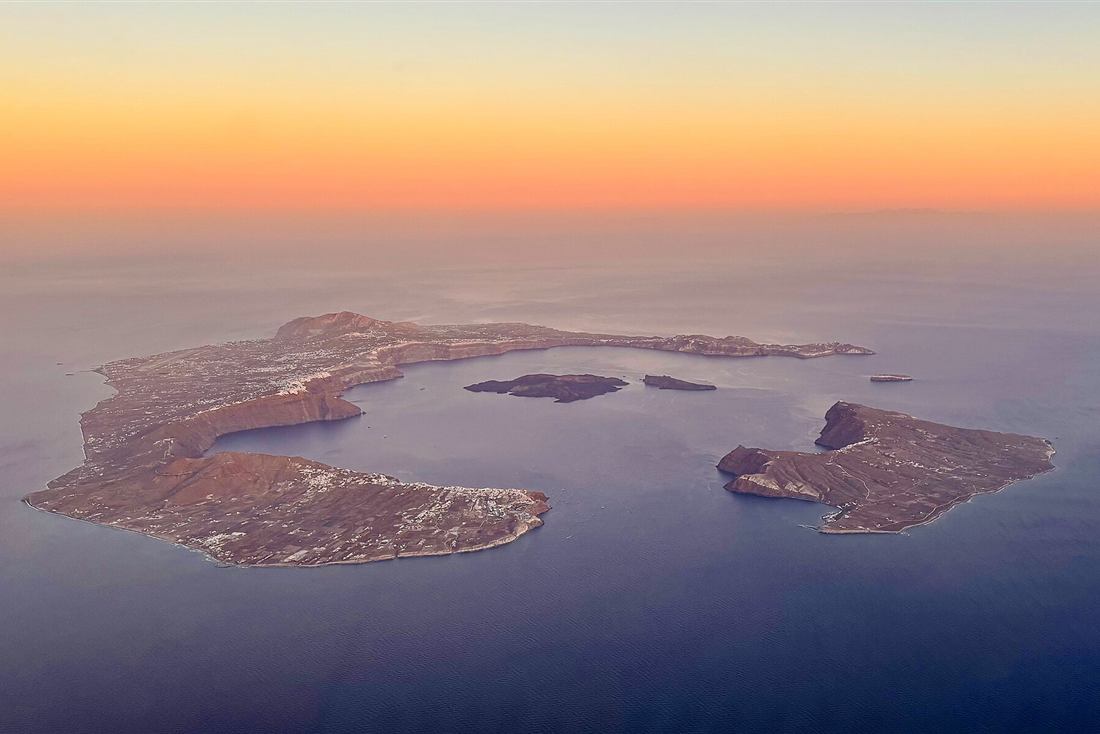 The whole Santorini caldera ring seen from the air at golden hour, the view a Santorini helicopter tour delivers