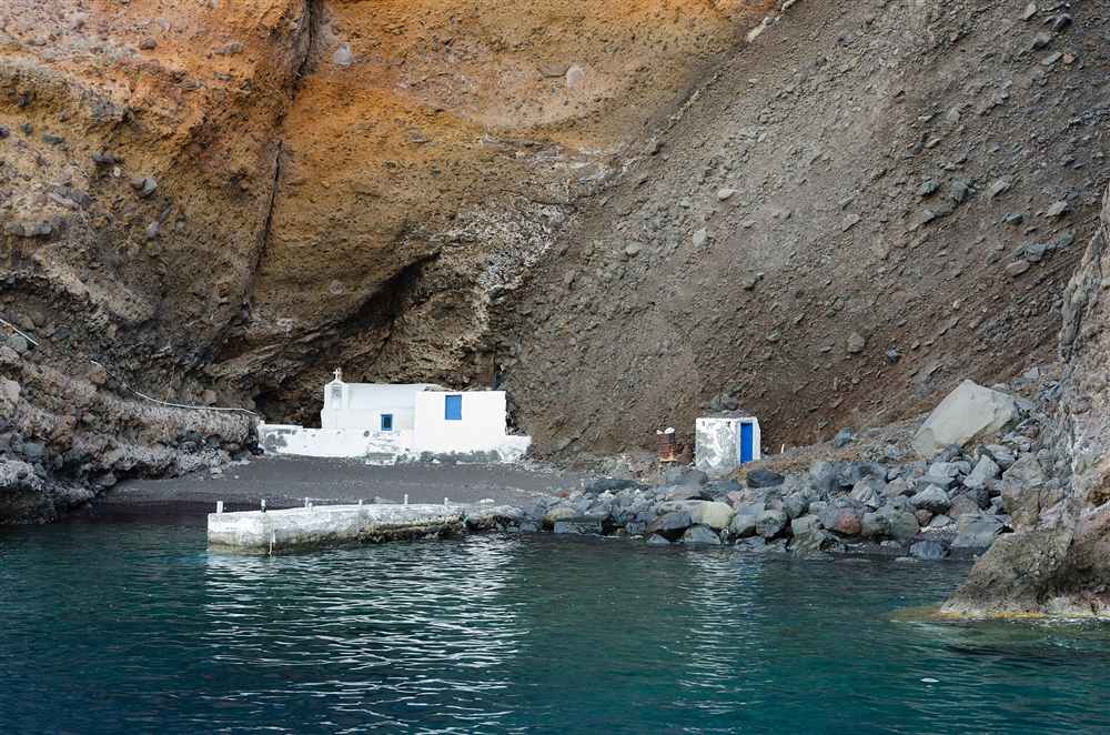 A whitewashed chapel at the waterline under the caldera cliffs of Santorini