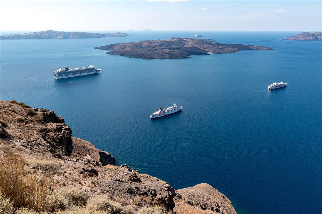 Cruise ships anchored in the Santorini caldera with the volcano island of Nea Kameni behind, the view from the rim on a shore excursion day