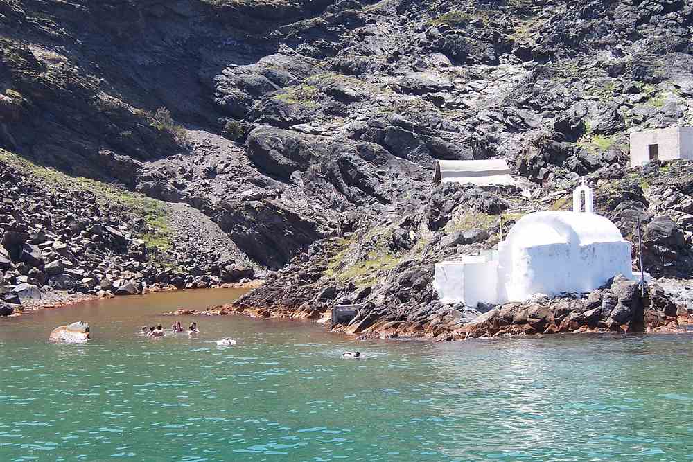 Swimmers in the ochre water at the Palea Kameni hot springs beside the white chapel, the swim stop on the caldera route