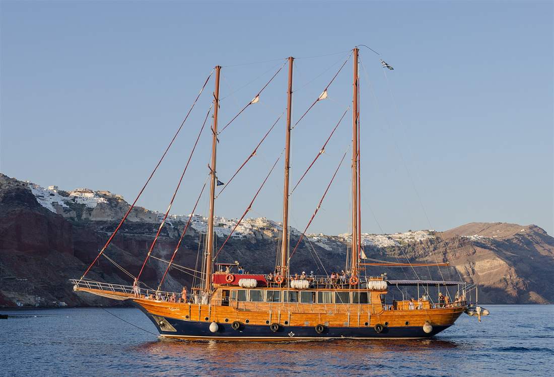 A sailing yacht cruising below the caldera cliffs and whitewashed town of Oia on a Santorini yacht charter