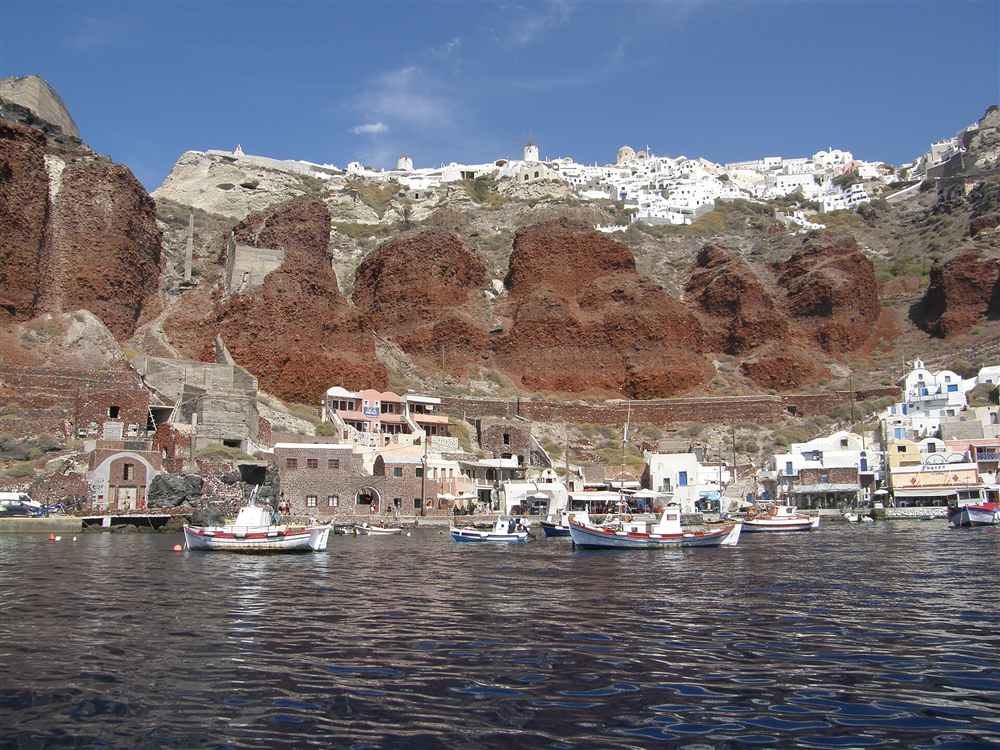 The red volcanic cliffs and boats of Ammoudi Bay below Oia, a Santorini yacht charter departure point