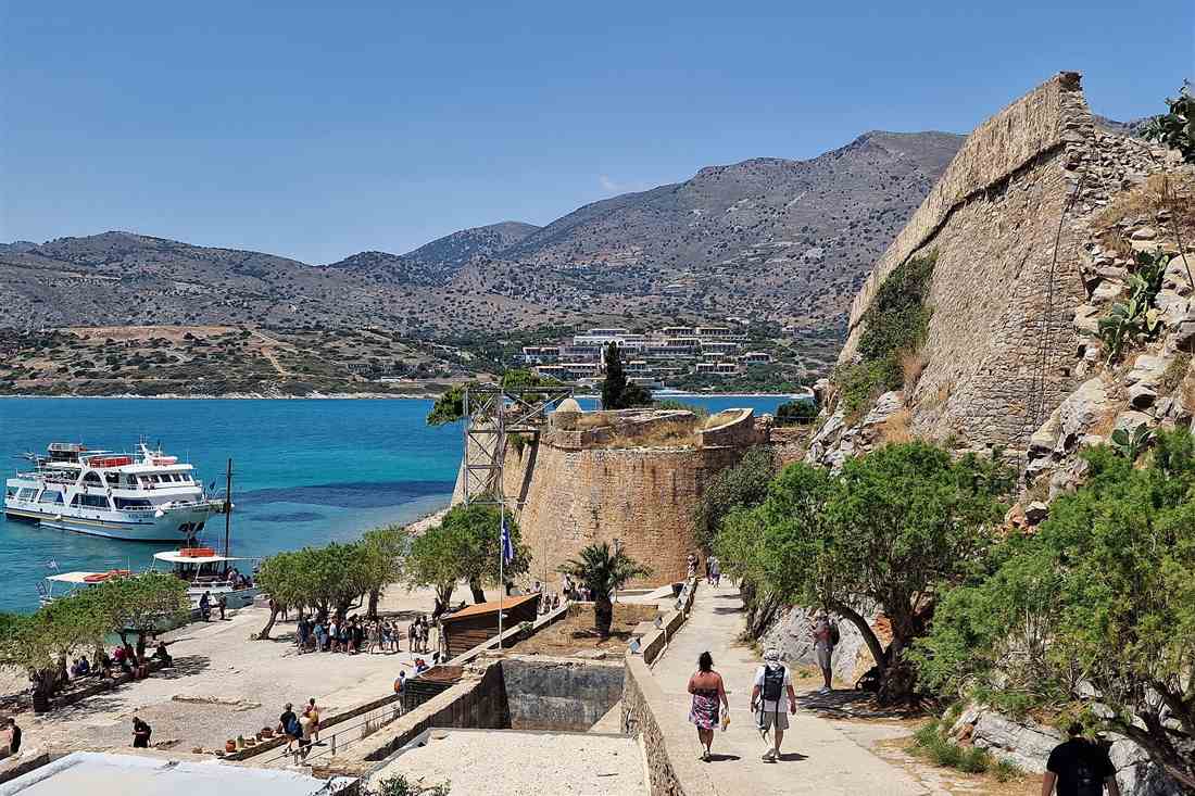 Spinalonga boat trip ferry at the island jetty below the Venetian walls with visitors walking the path