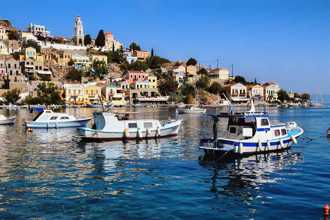 Symi e-bike tour: the pastel neoclassical houses of Gialos harbour climbing the hillside on Symi