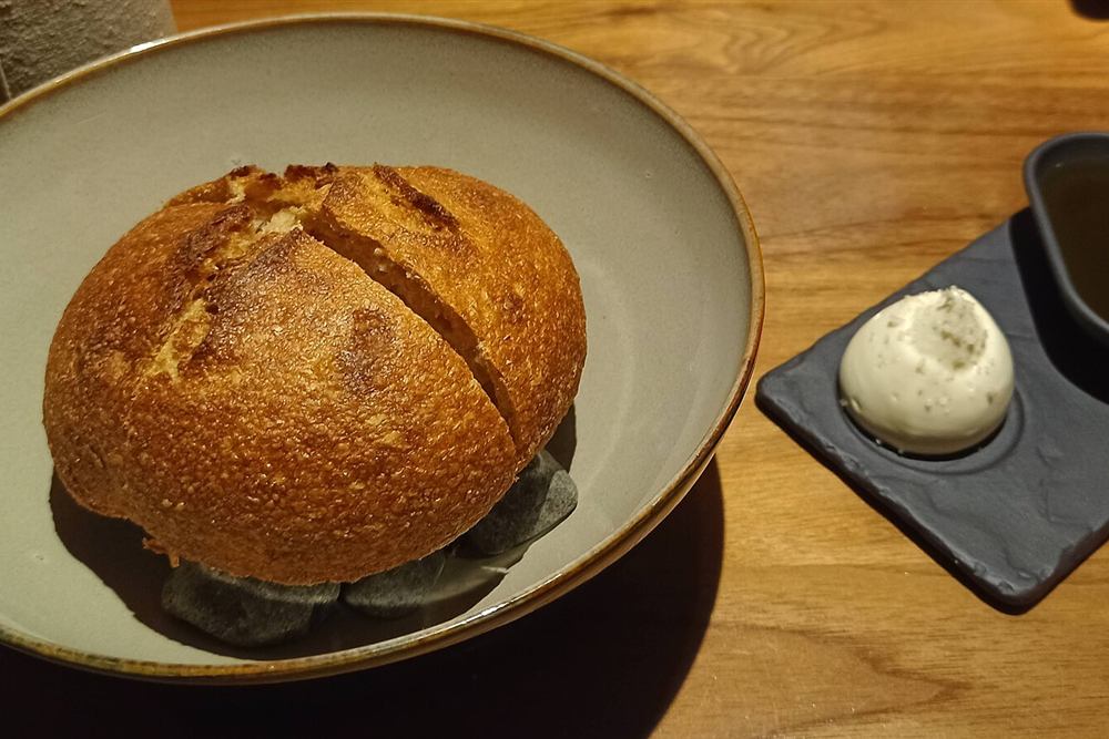 A loaf of bread served beside a dish of olive oil, the plate that comes with the wine at the producer