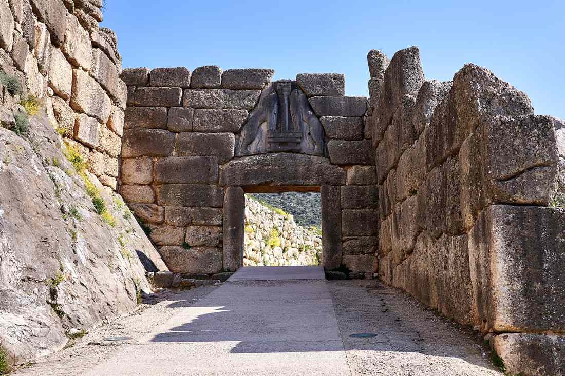 The Lion Gate of Mycenae, a stone gateway with two carved lions above the doorway, between massive stone walls under a blue sky