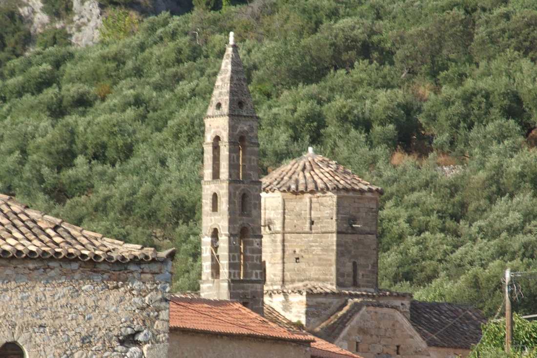 The stone bell tower and church of Agios Spyridon in Old Kardamyli, set against olive-covered slopes.