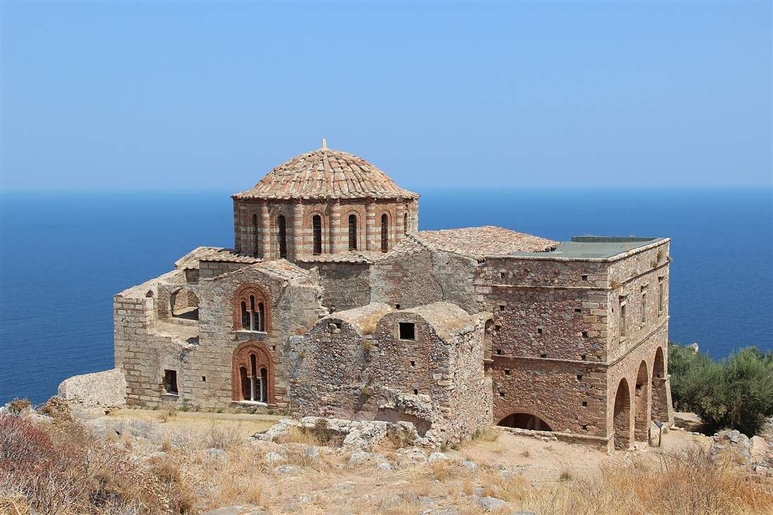 The Byzantine church of Agia Sofia on the clifftop of Monemvasia, with its tiled dome and stone walls above the deep blue sea.