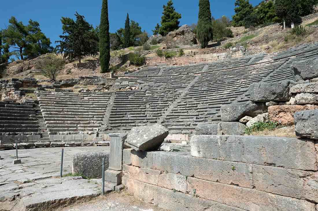 The stone seats of the ancient theatre of Delphi rising up the slope, with cypress and pine trees above.