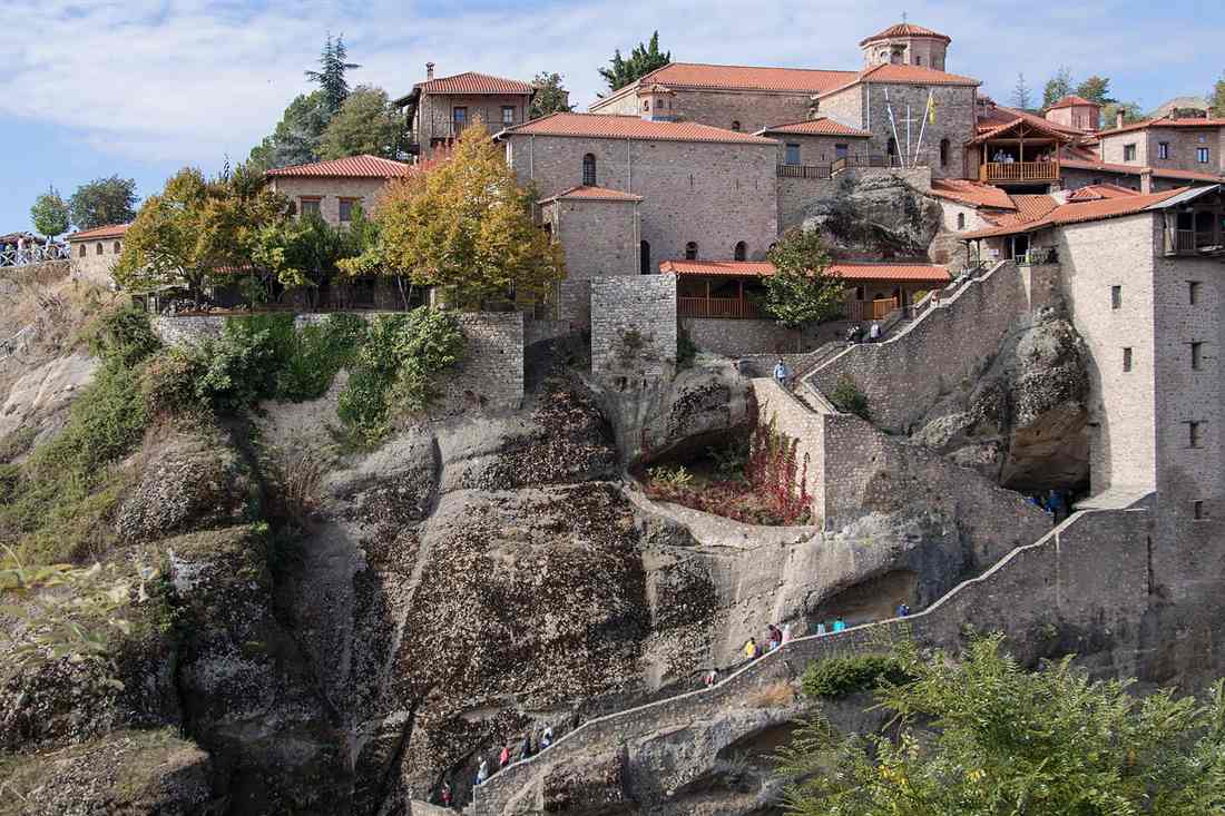 The Great Meteoron monastery on its rock pillar at Meteora, with stone stairs, red-tiled roofs and autumn trees.