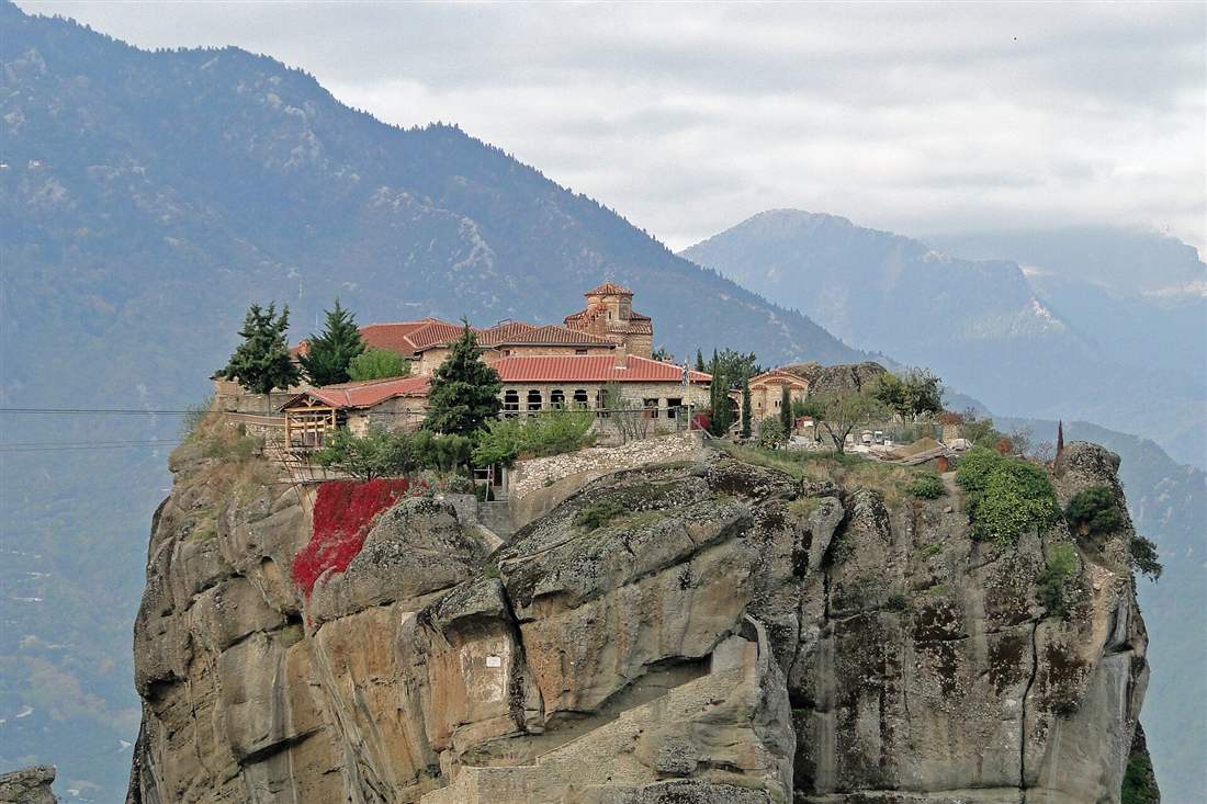 The Holy Trinity monastery on top of its sheer rock pillar at Meteora, with the Pindus mountains behind.