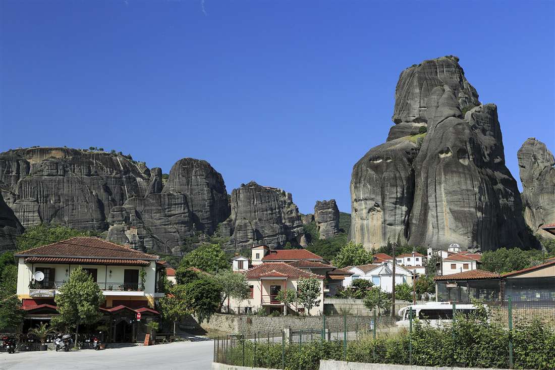 Giant grey rock pillars of Meteora rising above the houses of Kastraki under a clear blue sky.