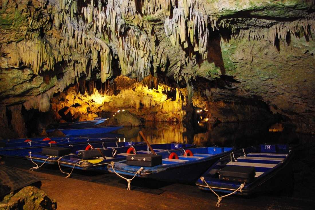 Small blue boats moored on the underground lake of the Diros caves, under lit stalactites.