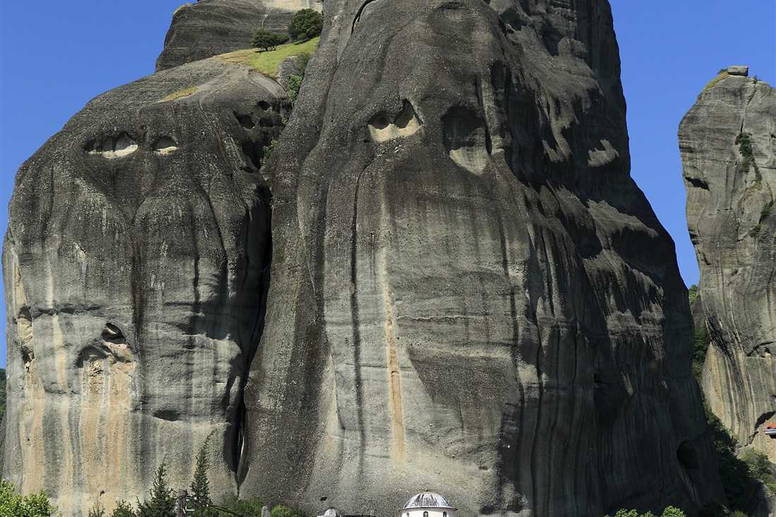 Houses of Kastraki at the foot of a huge grey rock pillar of Meteora under a deep blue sky.
