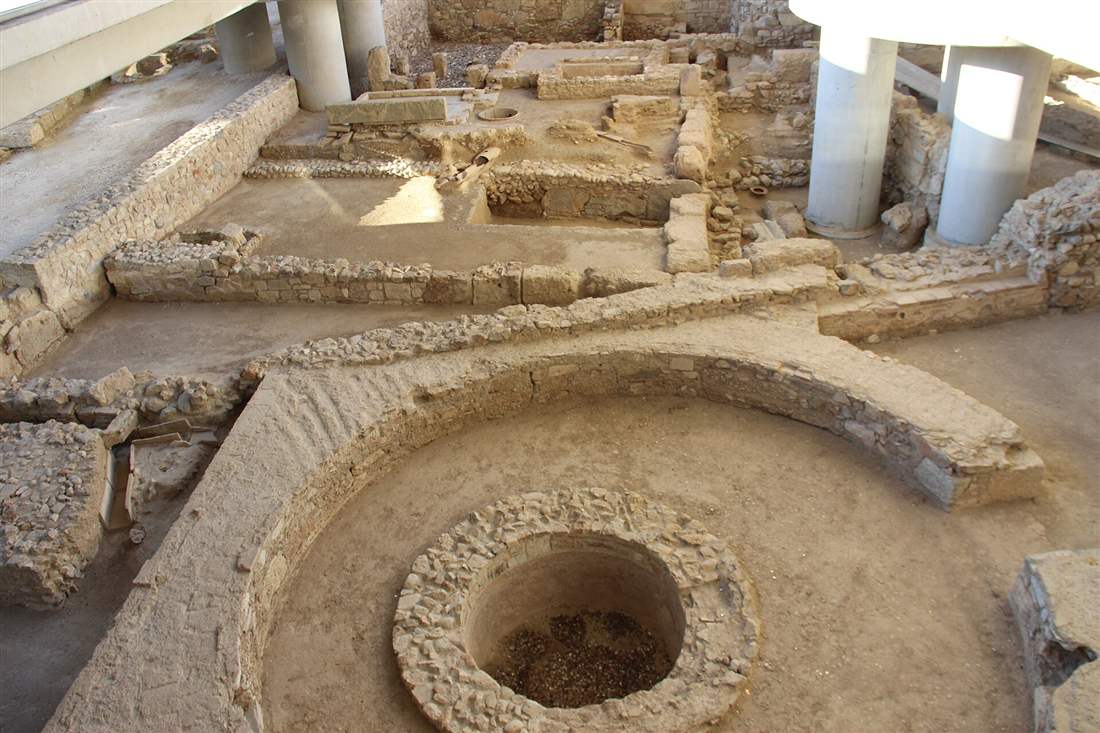 The excavated houses, walls and a round stone well of the ancient neighbourhood seen under the Acropolis Museum.