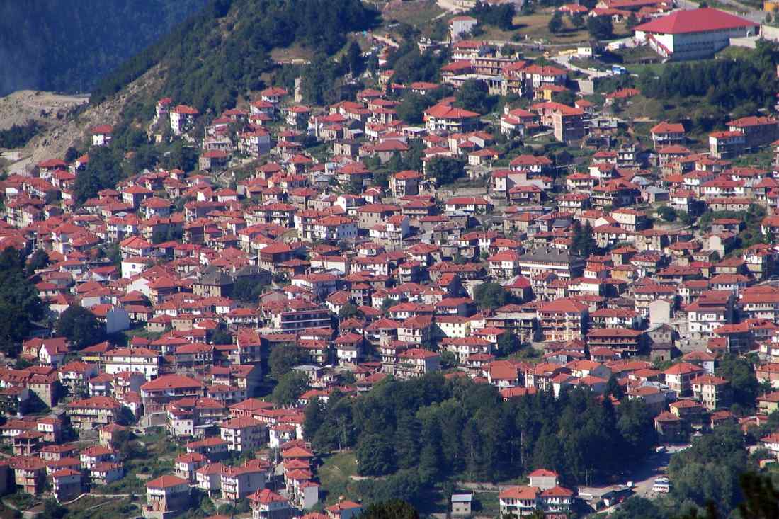 Stone houses with red tiled roofs covering the green mountain slope of Metsovo in the Pindos range.