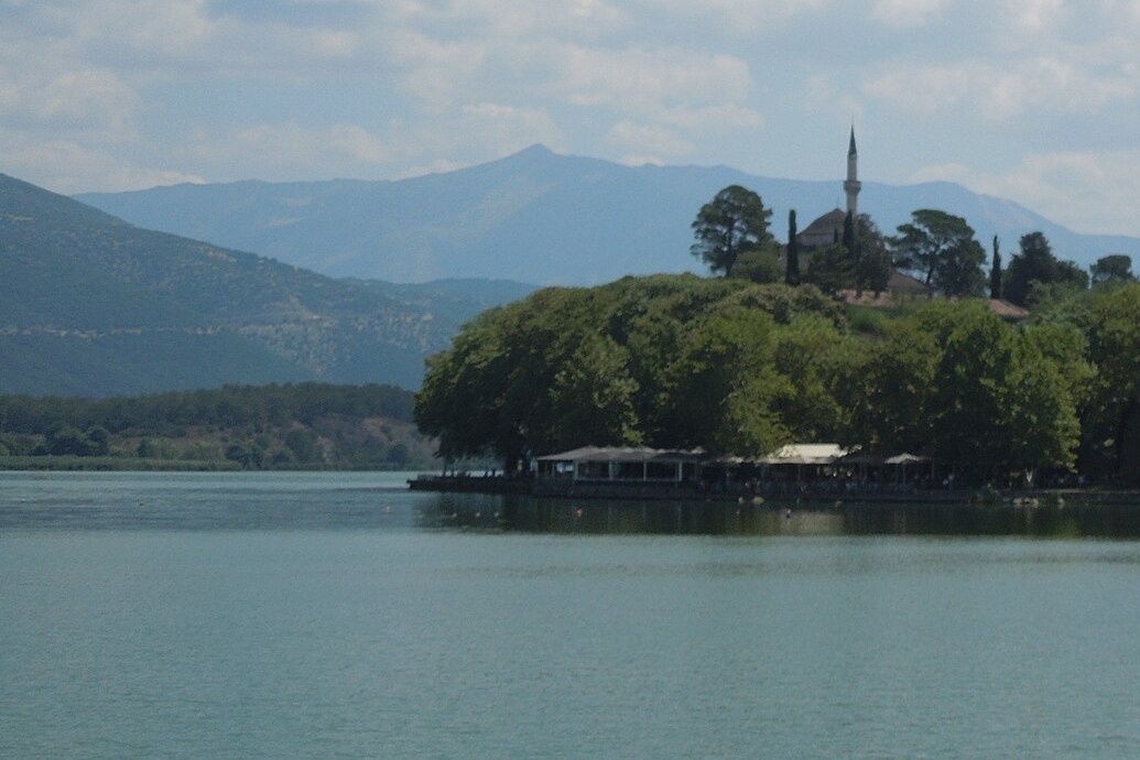 Lake Pamvotis at Ioannina, with the tree-covered castle headland and the minaret of the Aslan Pasha Mosque above the water and mountains behind.