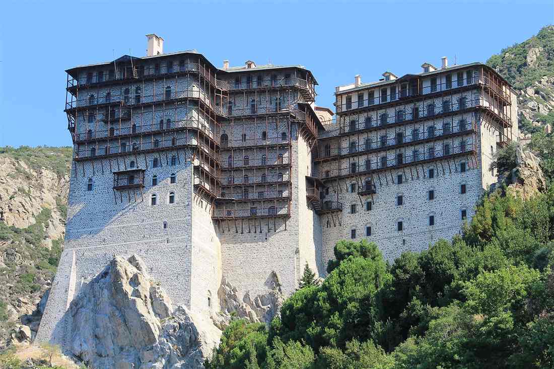 The Simonopetra monastery rising from its rock above the forest on Mount Athos under a clear blue sky.