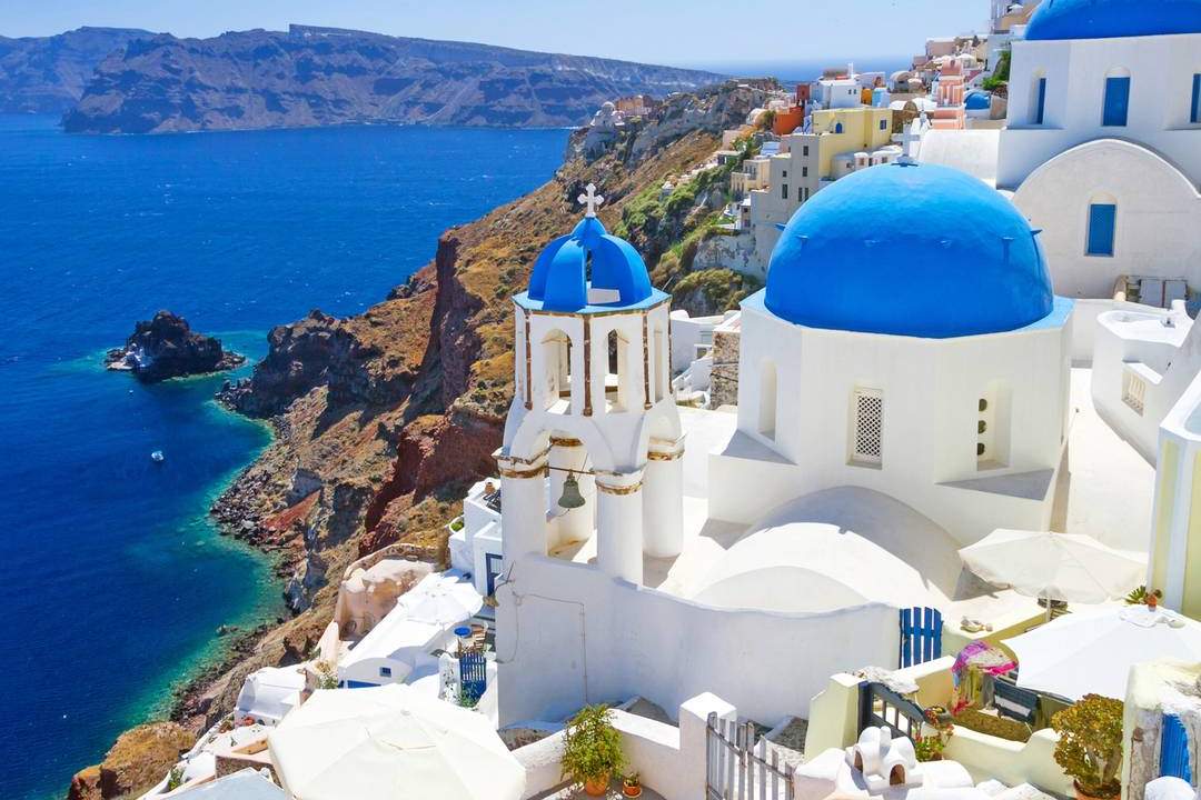 Blue-domed churches and white houses of Oia above the Santorini caldera, with the deep blue Aegean Sea below.