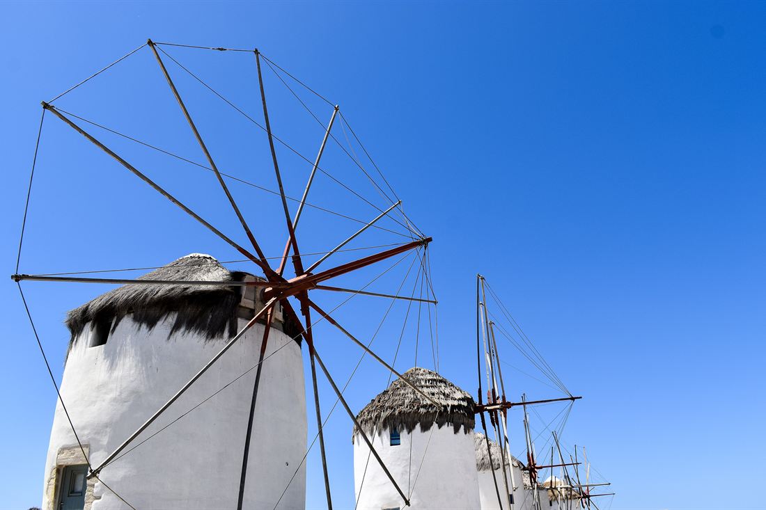 White windmills with thatched roofs and wooden sail frames under a clear blue sky