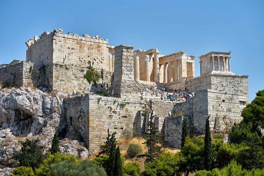 The Propylaea gateway and the small Temple of Athena Nike on the Acropolis bastion, seen from below against a clear blue sky