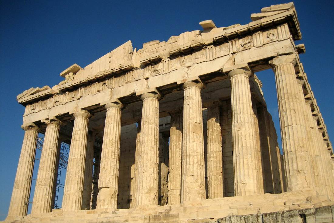 West front of the Parthenon on the Acropolis in Athens, its Doric columns and carved beam lit by warm sun against a clear blue sky