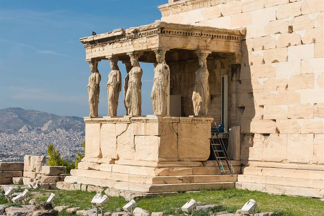 Caryatid Porch of the Erechtheion on the Acropolis, with the maiden statues holding up the roof and Athens in the distance