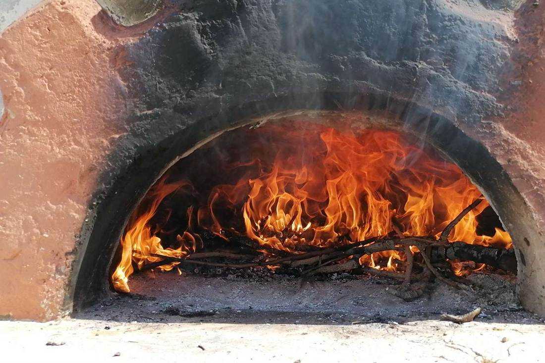 Flames burning inside a traditional wood-fired clay oven with sticks of firewood on the oven floor