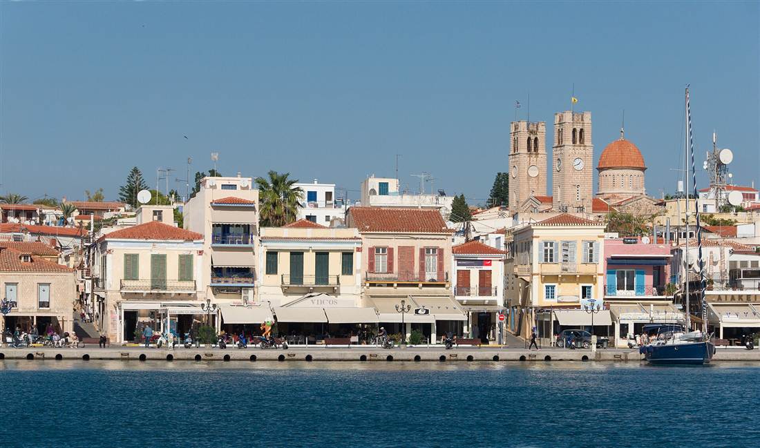 Aegina Town harbour front with neoclassical buildings and the twin bell towers of the cathedral above moored boats