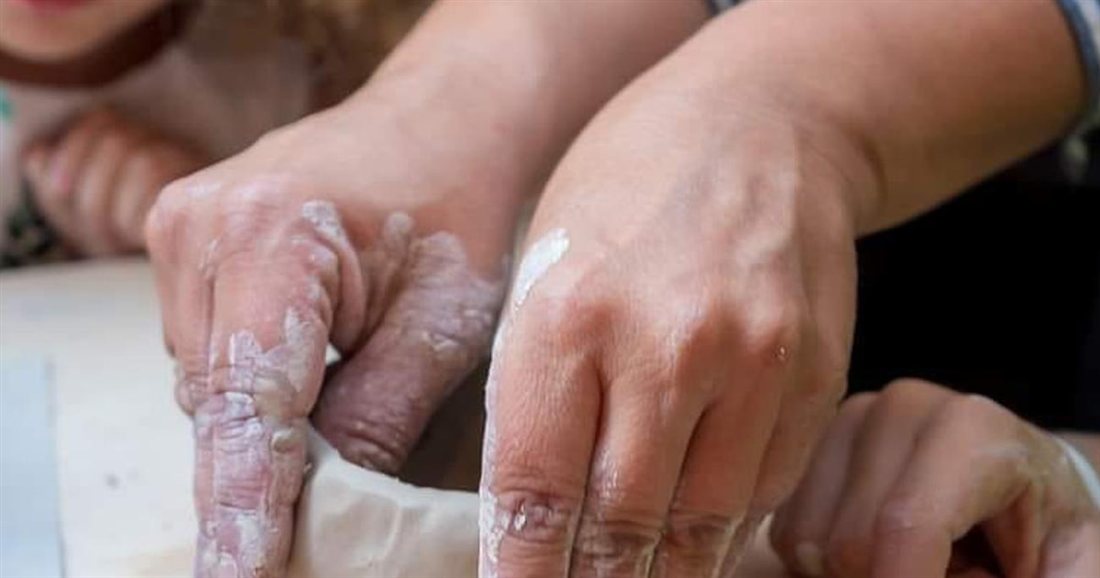 Hands pinching and shaping a lump of clay into a small pot at an Aegina pottery class.