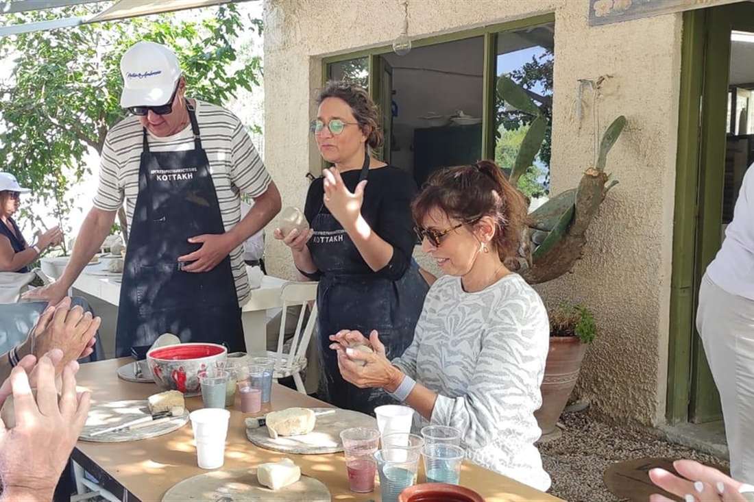 Guests shaping clay at an outdoor table while the potter shows them how, at an Aegina pottery class.