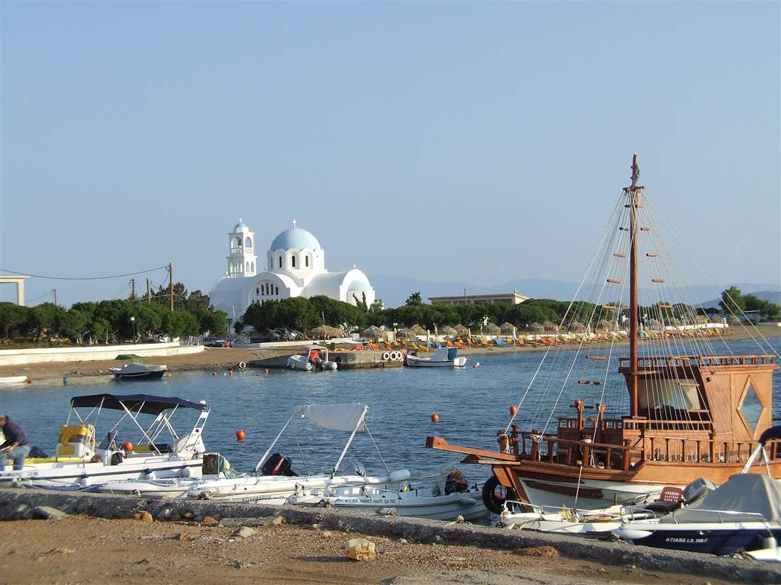 A wooden caique and small boats in the harbour of Skala below the white church of Agioi Anargyroi, where an Agistri boat trip calls.