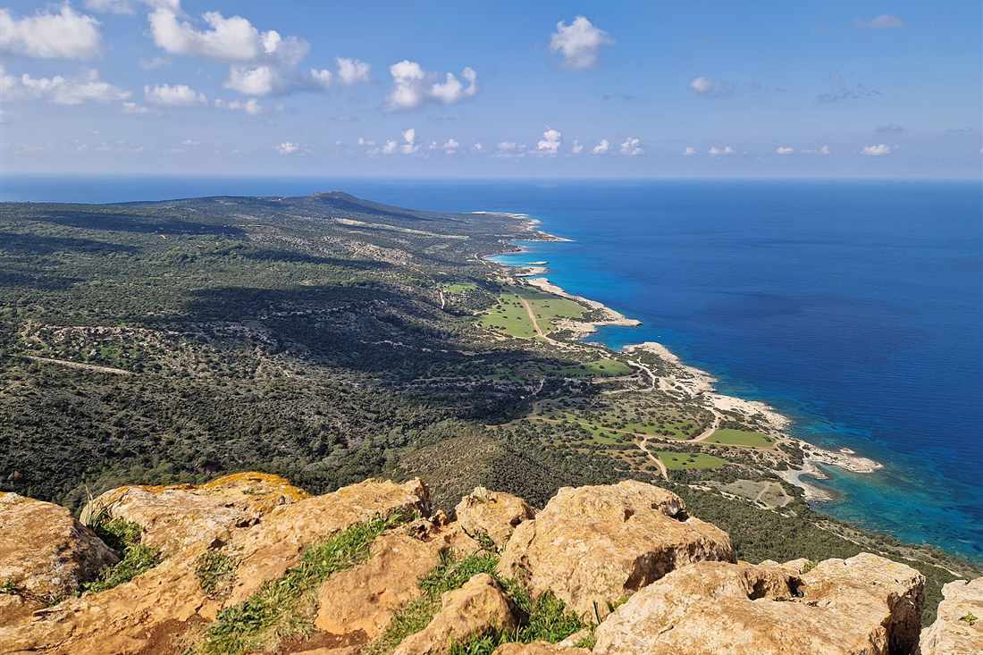 Aerial view of the Akamas peninsula coastline with green hills and deep blue sea seen from a rocky lookout