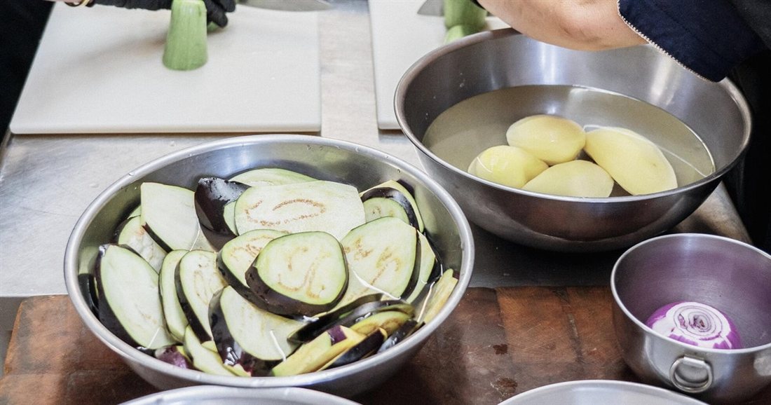 Bowls of sliced aubergine, peeled potatoes and chopped red onion ready for cooking in an Amorgos cooking class.