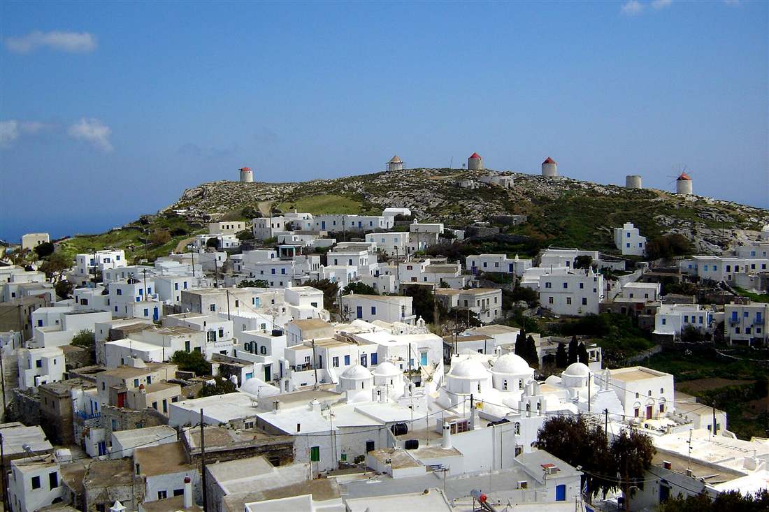 Whitewashed houses of Chora on Amorgos below a hill lined with old windmills under a blue sky