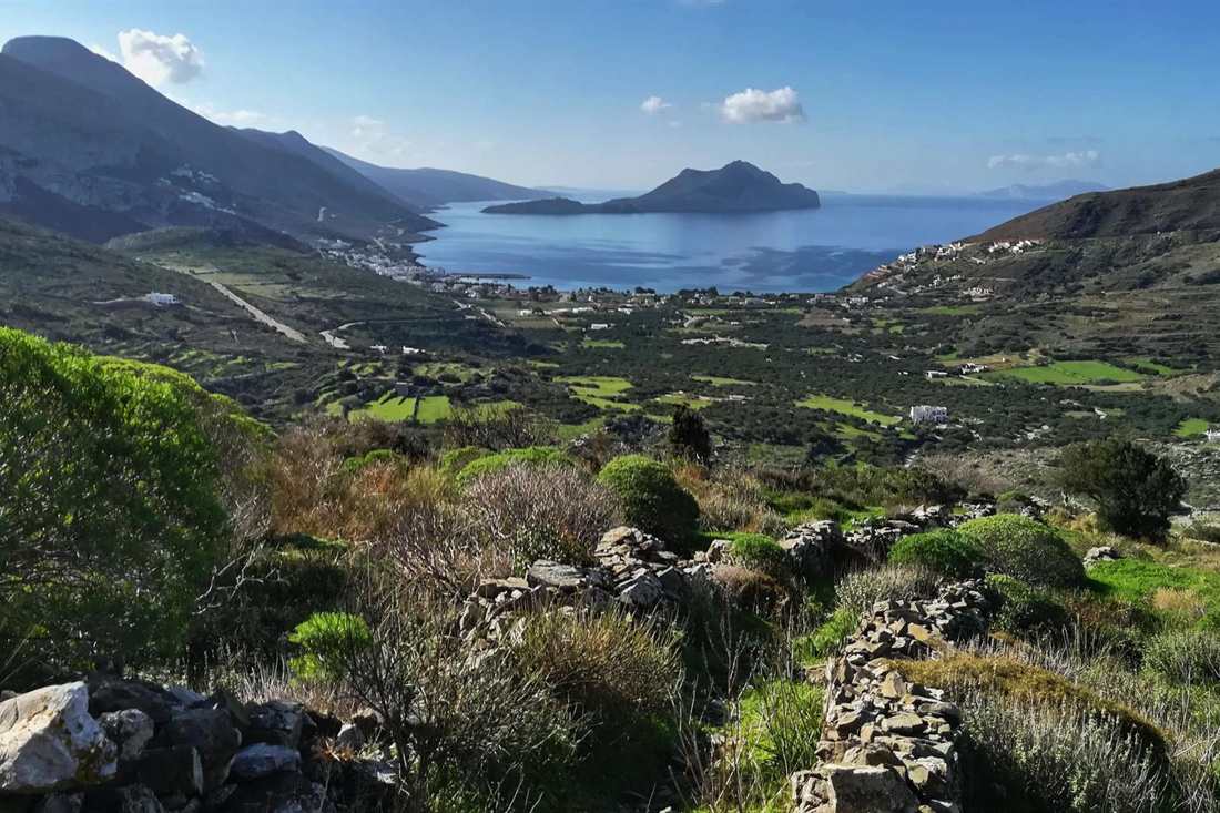 Dry-stone terrace walls and green fields running down a valley to a bay with a rocky islet off Amorgos