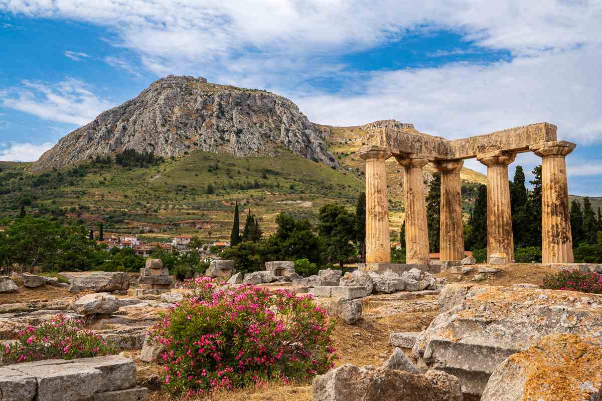 An Ancient Corinth tour stops at the Doric columns of the Temple of Apollo, which stand among flowering oleanders below the rock of Acrocorinth.