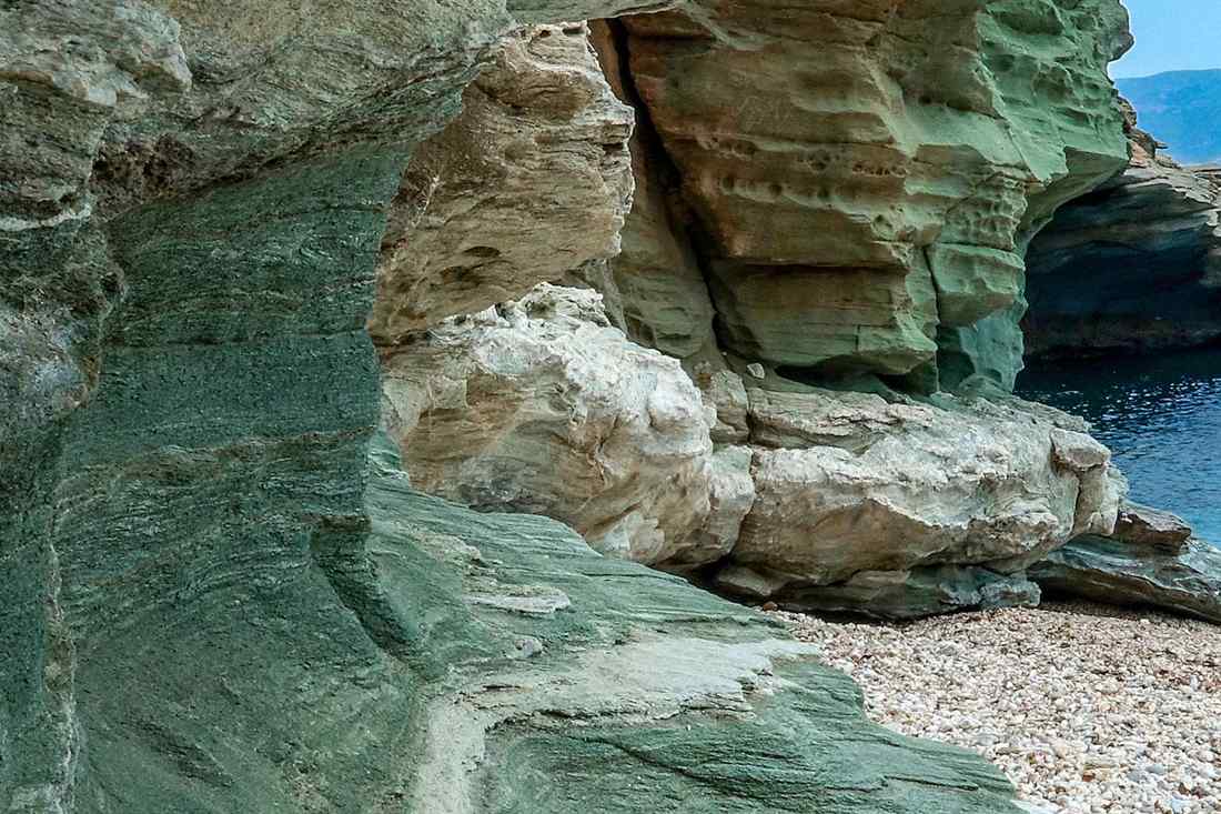 Green and white rock formations above a pebble beach on the coast of Andros