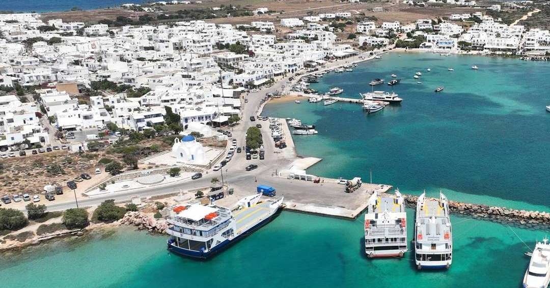 Aerial view of Antiparos town with white houses, the harbour, moored ferries and turquoise water.