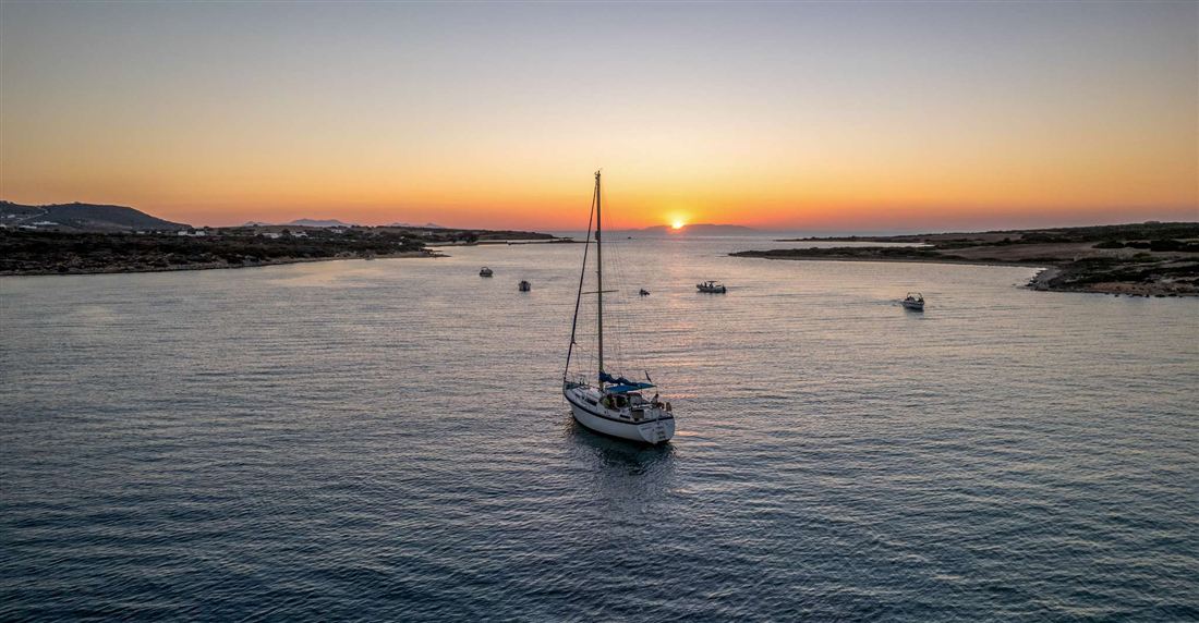A sailing yacht anchored in a calm bay off Antiparos as the sun sets behind low hills