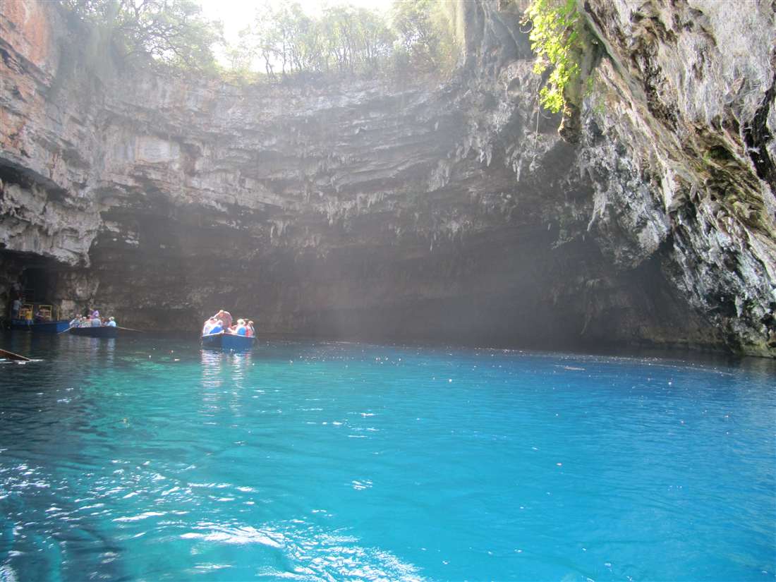 Rowing boats on the turquoise lake of the Melissani cave under its open roof, a stop on an Argostoli private tour.