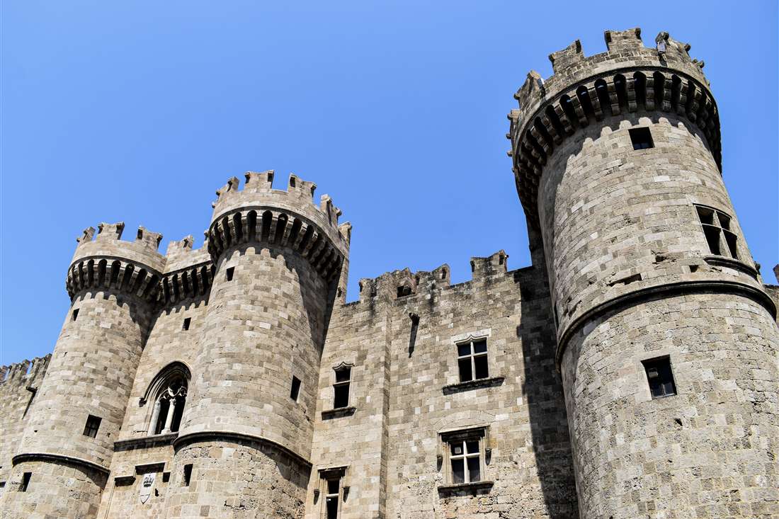 Stone towers and crenellated walls of the Palace of the Grand Master of the Knights in Rhodes under a clear blue sky