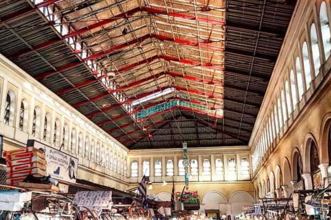 Inside the Athens Central Market hall with red iron roof trusses, arched windows and market stalls below